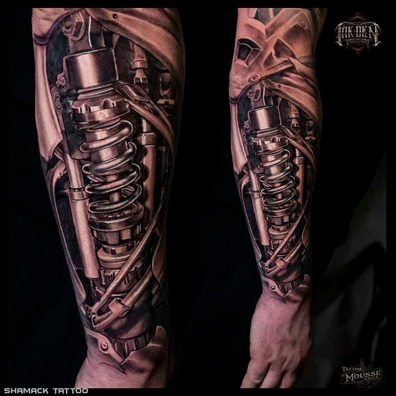Close-up of a metallic biomechanical tattoo on an arm, showing chrome springs, gears, and tubing.
