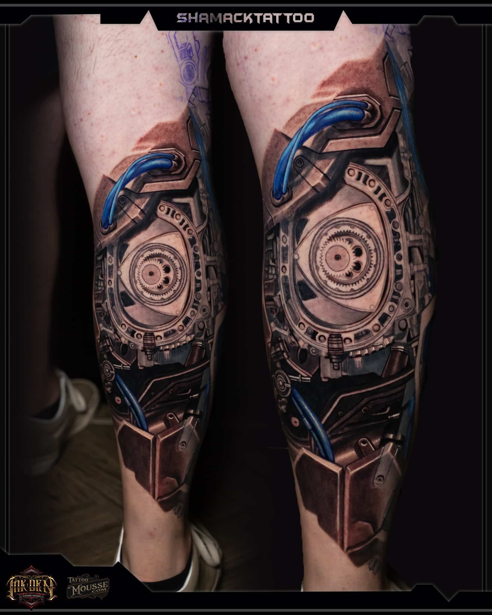 Pair of tattooed lower legs with matching circular mechanical designs and blue accents.