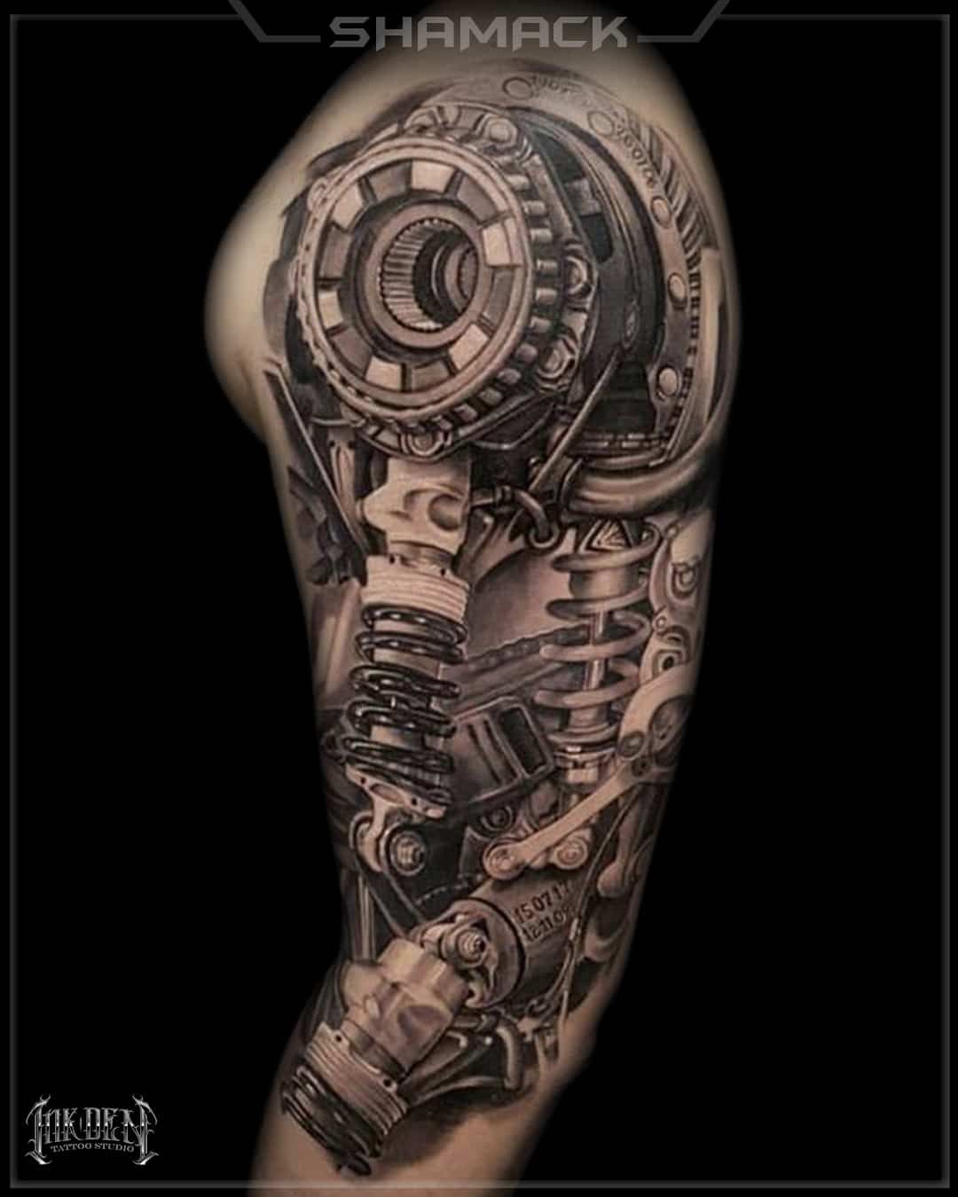 Black and gray biomechanical tattoo design on a human arm, with a mechanical circular detail near the shoulder.